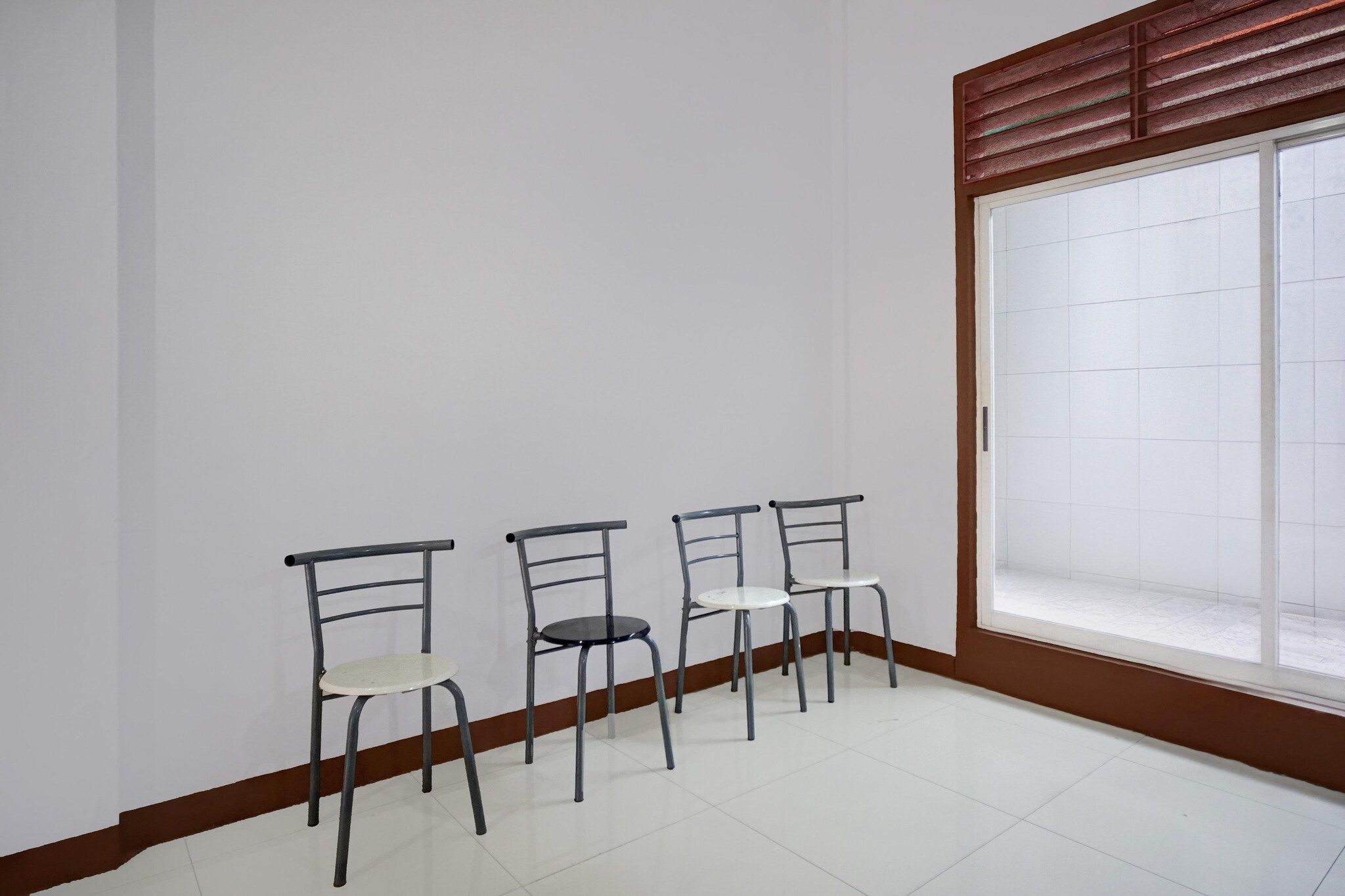 A room with three metal chairs and a large window with blinds.