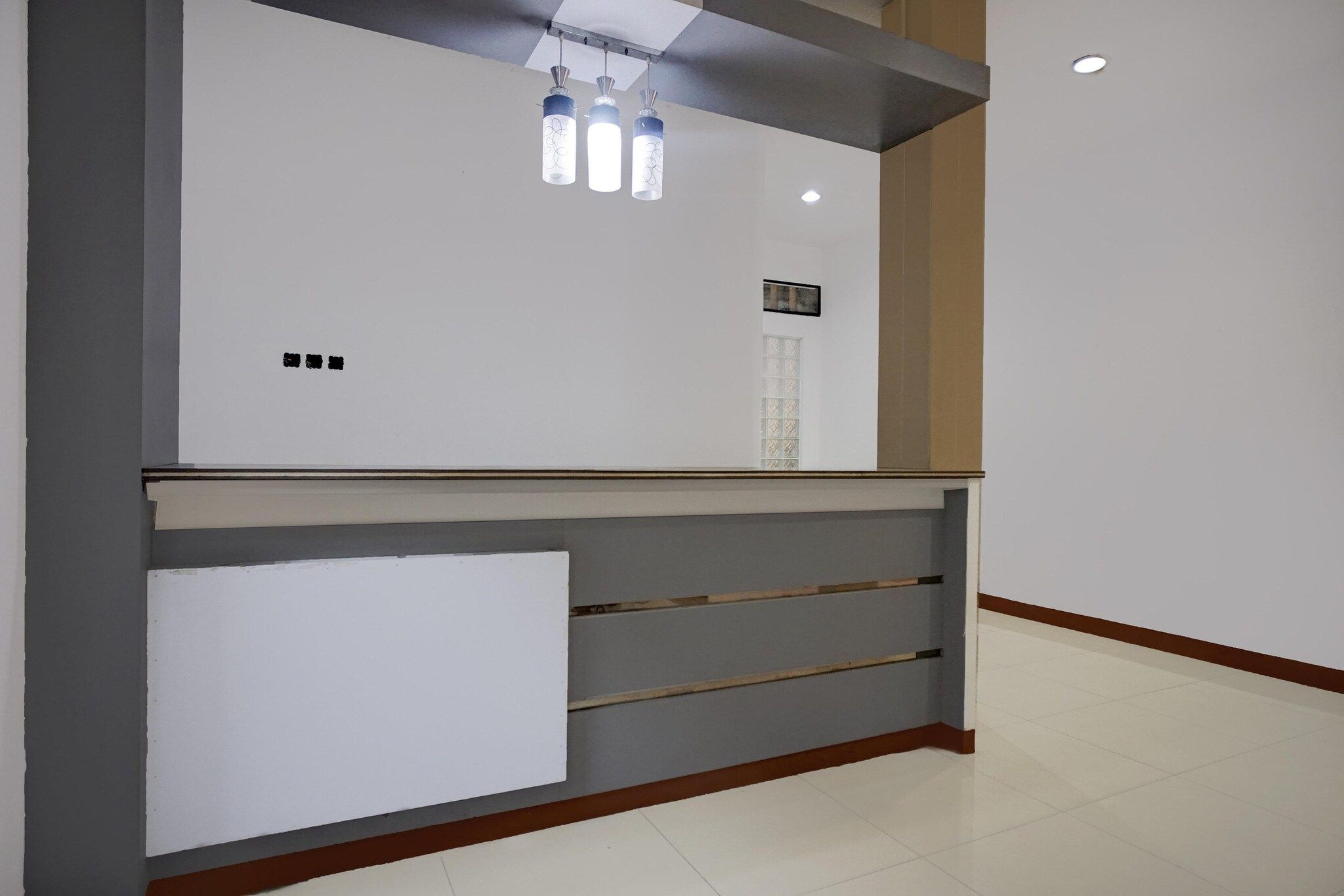 A reception desk with a white panel, three pendant lights, and a small window.