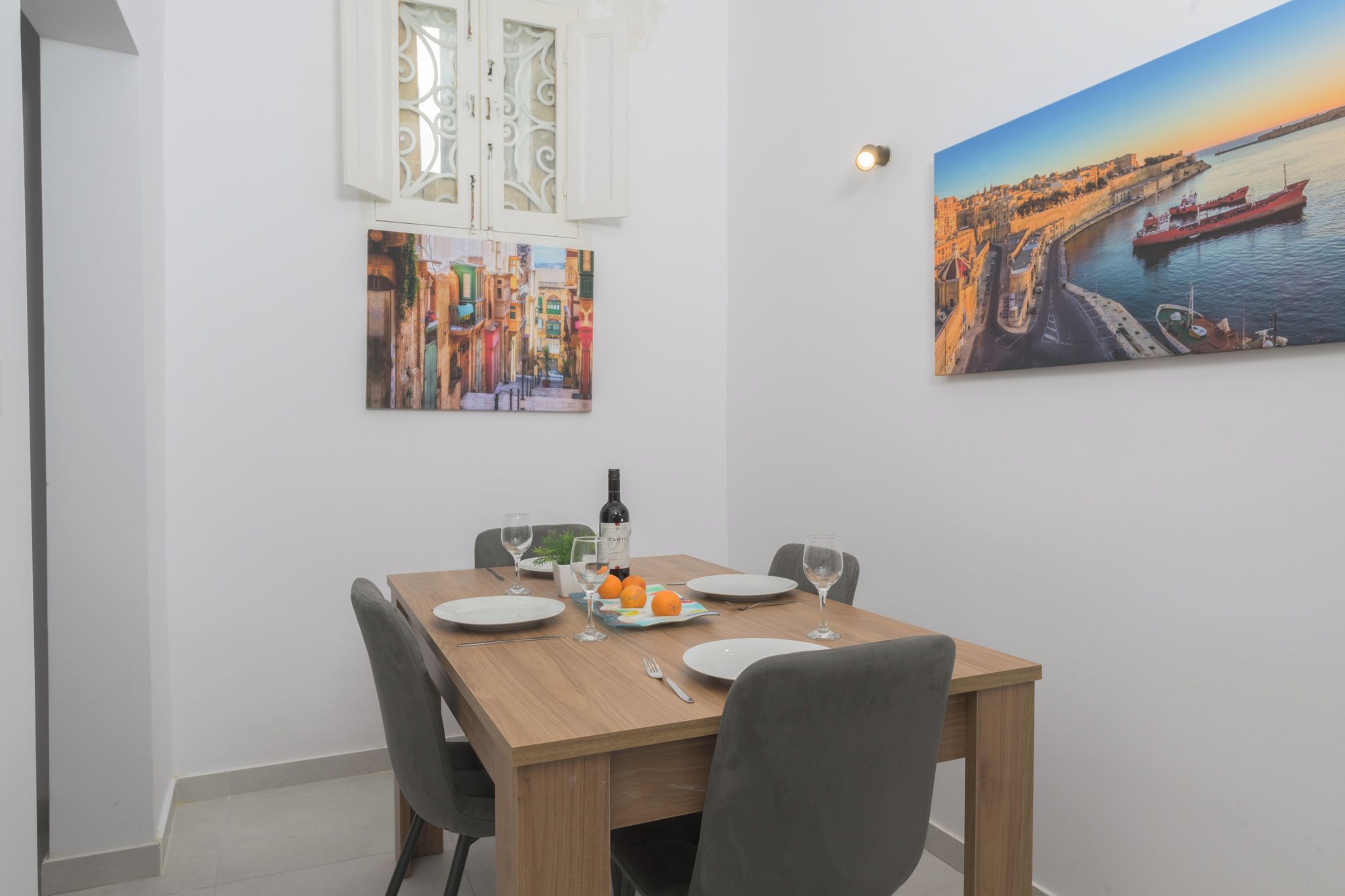 Un comedor con una mesa de madera dispuesta para dos personas, dos sillas, una botella de vino y dos copas.
