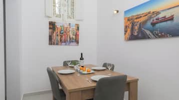 Un comedor con una mesa de madera dispuesta para dos personas, dos sillas, una botella de vino y dos copas.