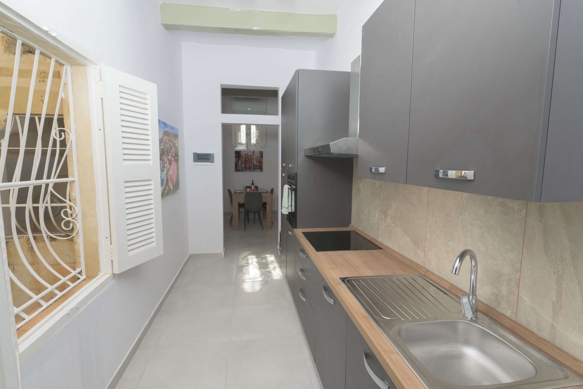 A narrow kitchen with a sink, cabinets, and a dining area in the background.