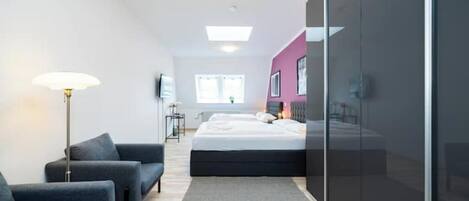 A modern bedroom with a bed, a seating area with chairs, a floor lamp, and a large window.