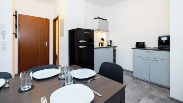 Un coin repas avec une table dressée pour quatre personnes, une kitchenette équipée d’une cuisinière et d’un four à micro-ondes, et une porte donnant sur une autre pièce.