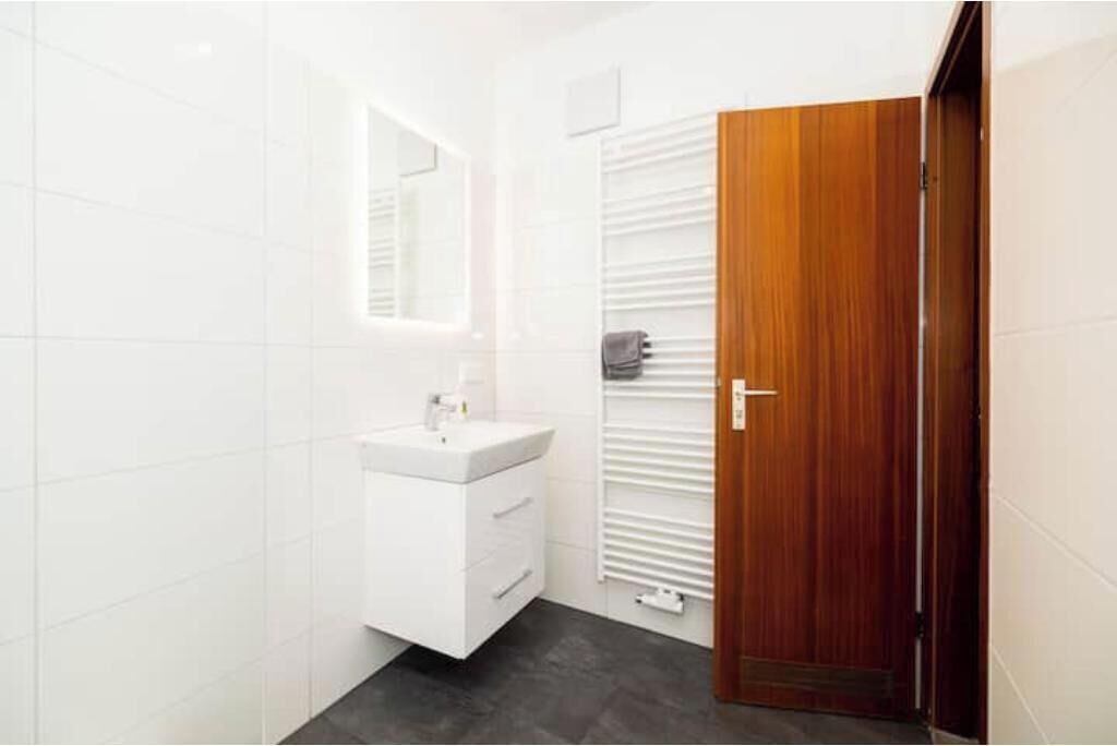 Um banheiro com toucador branco, espelho, porta-toalhas e porta de madeira.