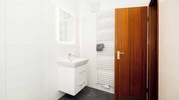 Um banheiro com toucador branco, espelho, porta-toalhas e porta de madeira.