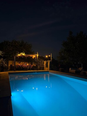 Ein Schwimmbecken bei Nacht mit Lichterketten und einer überdachten Sitzgelegenheit.