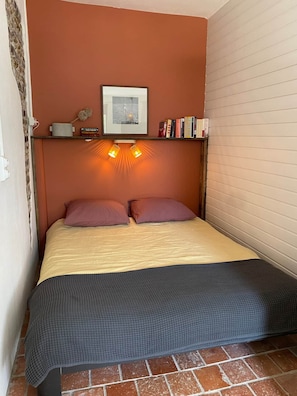 Ein Bett mit Kopfteil, ein Bücherregal, ein gerahmtes Bild und zwei Wandleuchten.