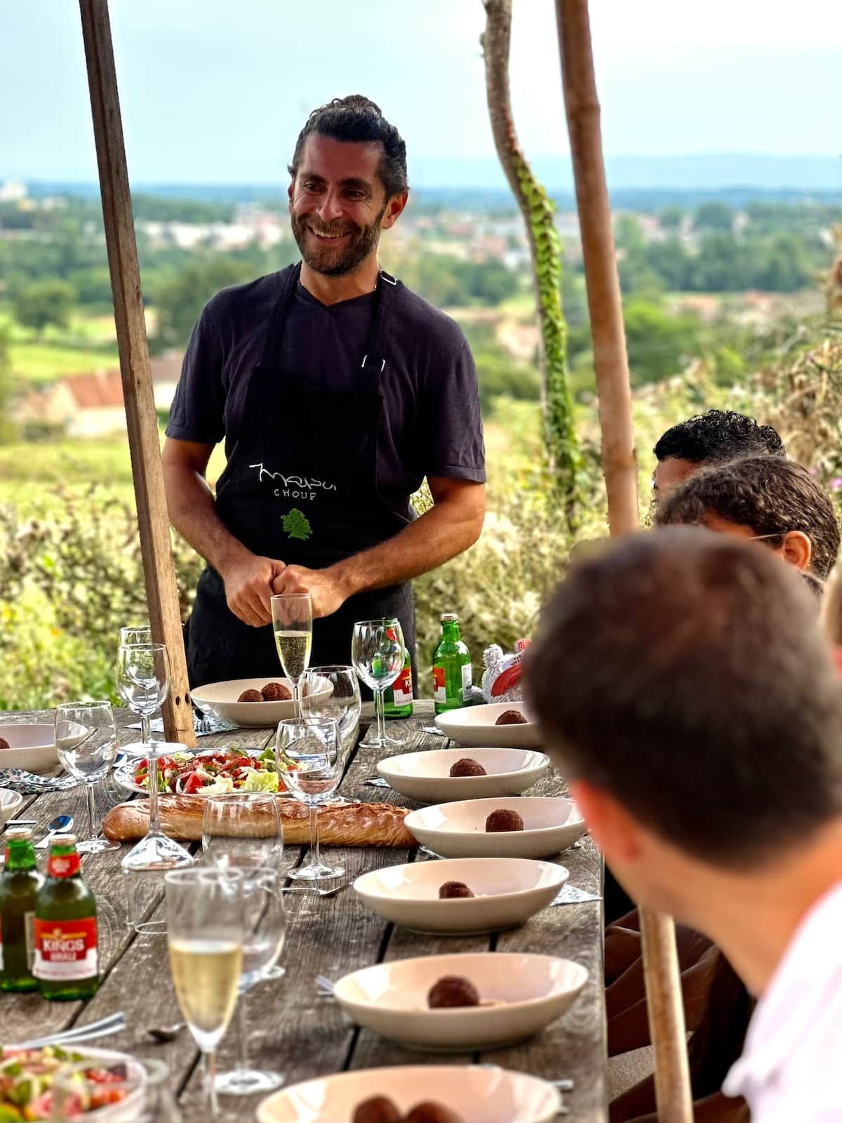 Une personne servant des plats à une table en plein air, avec une vue panoramique.