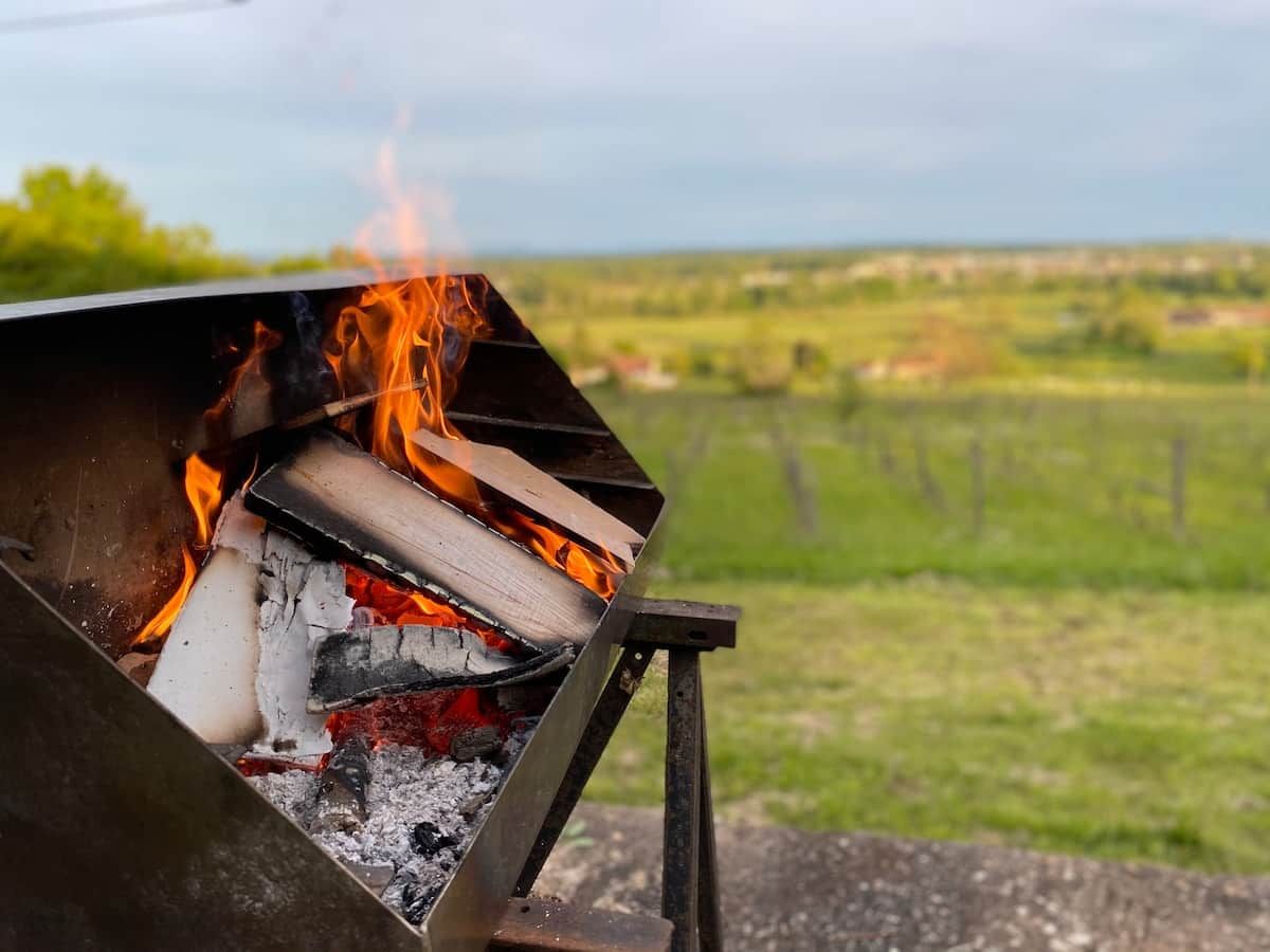 Ein Grill mit Flammen vor einer ländlichen Landschaft.