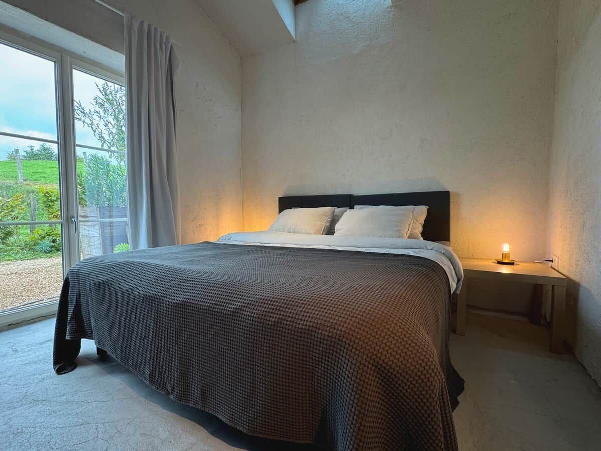 Een slaapkamer met een bed, nachtkastjes en uitzicht door een groot raam.