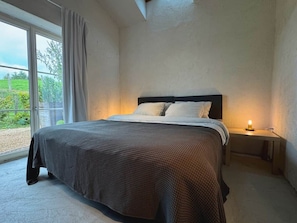 Une chambre à coucher avec un lit, des tables de chevet et une vue sur l’extérieur grâce à une grande fenêtre.