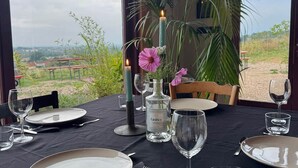 Ein Esstisch, gedeckt für vier Personen, mit Kerzen, einer Flasche GinBey und Blick auf die Landschaft.