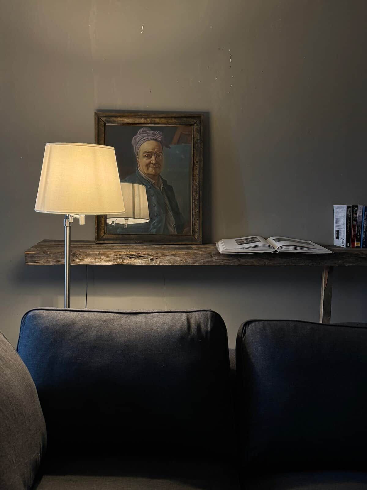 Una habitación con una lámpara, un retrato enmarcado, un libro y una estantería llena de libros.