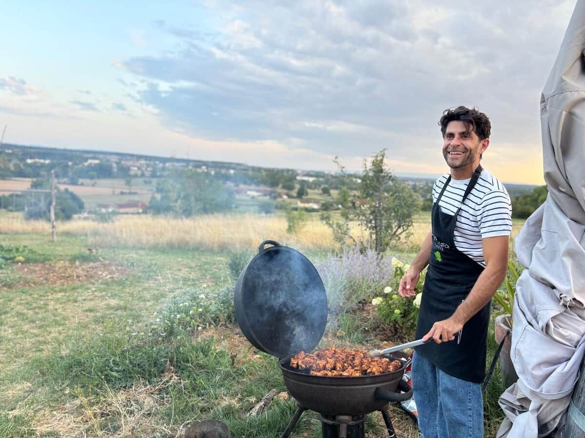 A person grilling outdoors with a view of a rural landscape.