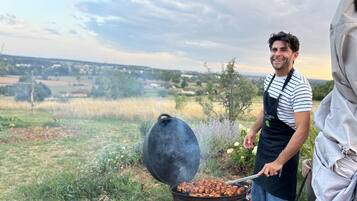A person grilling outdoors with a view of a rural landscape.