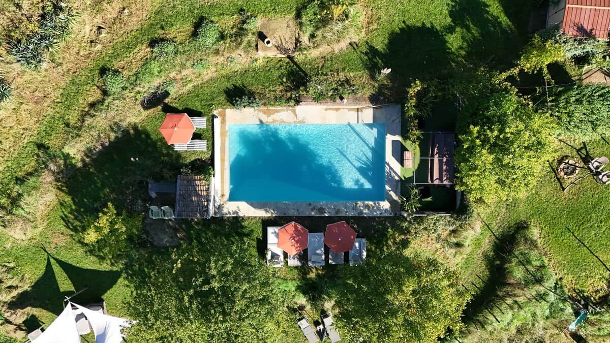 Vista aérea de una propiedad con piscina, rodeada de vegetación y una zona vallada.