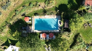 Vue aérienne d’une propriété dotée d’une piscine, entourée de verdure et d’une zone délimitée par une clôture.