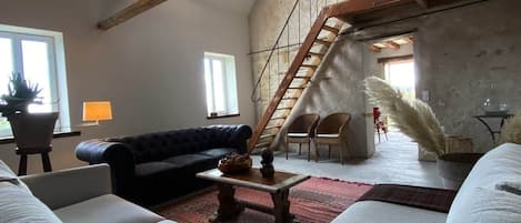 A spacious living area with a high ceiling, a staircase, and a view of the outdoors.