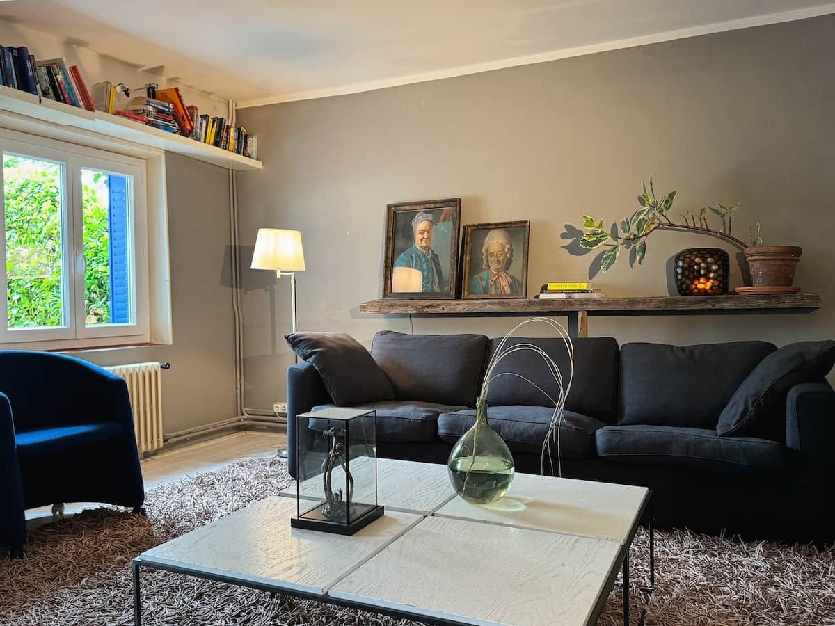 En stue med sofa, sofabord og lampe. Reoler og et vindue med udsigt.