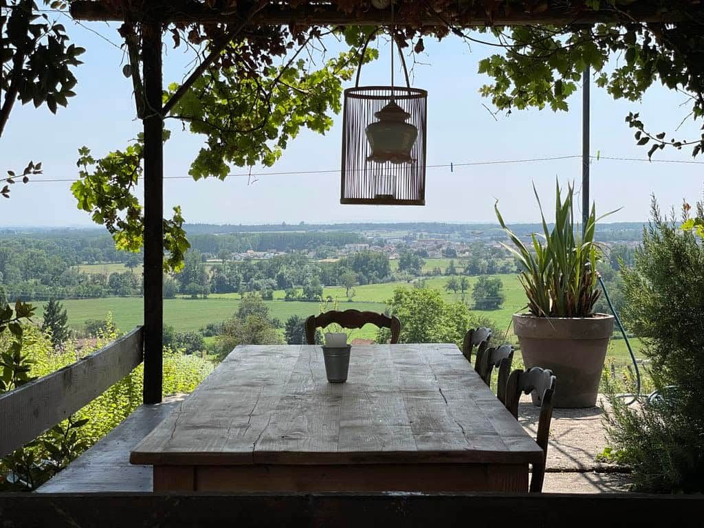Ein Essbereich im Freien mit Tisch und Stühlen, einer hängenden Laterne und Blick auf eine grüne Landschaft.