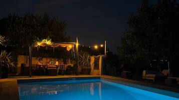 A swimming pool at night with string lights and a covered seating area.