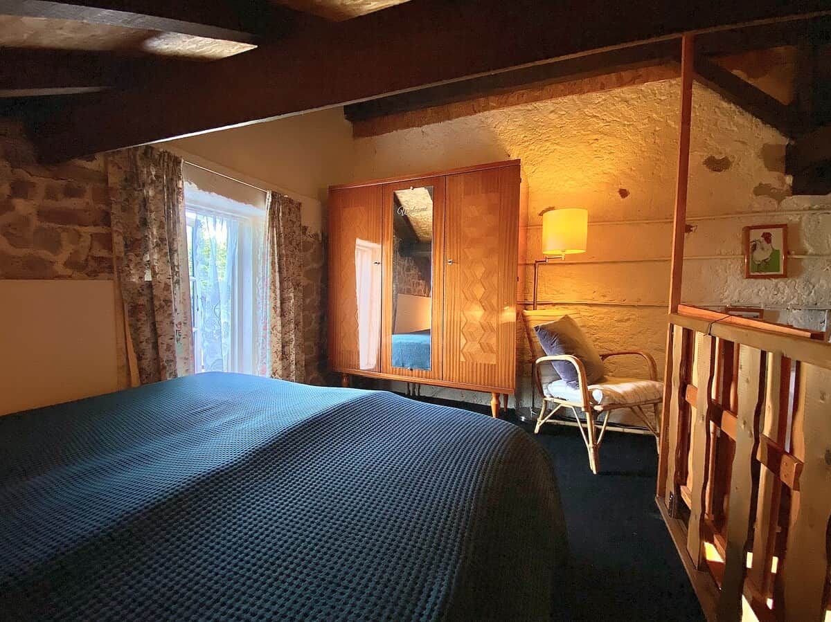 Une chambre à coucher avec un lit, une armoire en bois, une chaise et une fenêtre avec des rideaux.