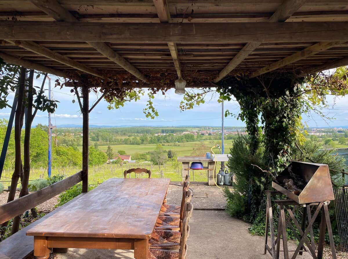 Ein Essbereich im Freien mit Tisch und Stühlen, einem Grill und Blick auf die Landschaft.