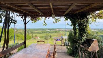 Ein Essbereich im Freien mit Tisch und Stühlen, einem Grill und Blick auf die Landschaft.