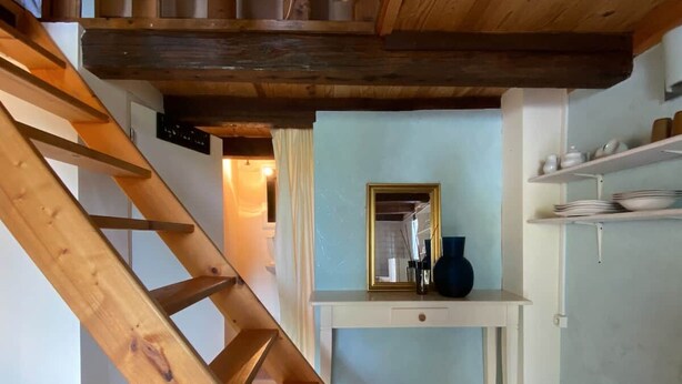 Una escalera que lleva a una habitación con un espejo, un jarrón y estantes con platos.