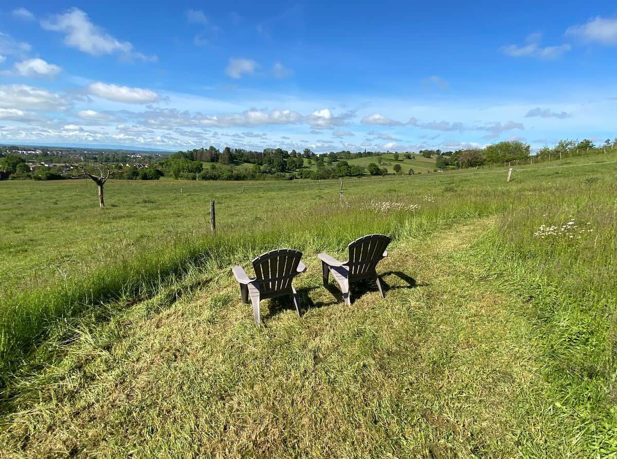 Een open veld met twee Adirondack-stoelen gericht op een uitzicht op een stad in de verte.