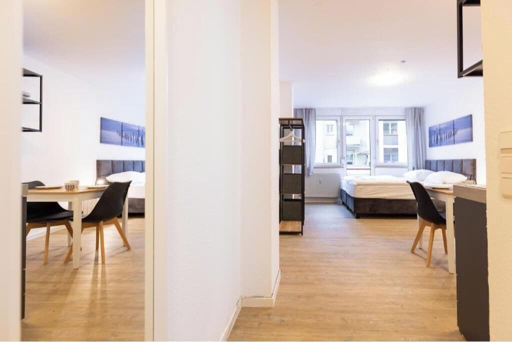 Een moderne hotelkamer met een houten vloer, een bed met een grijze hoofdbord, een bureau met een stoel en een garderobe.