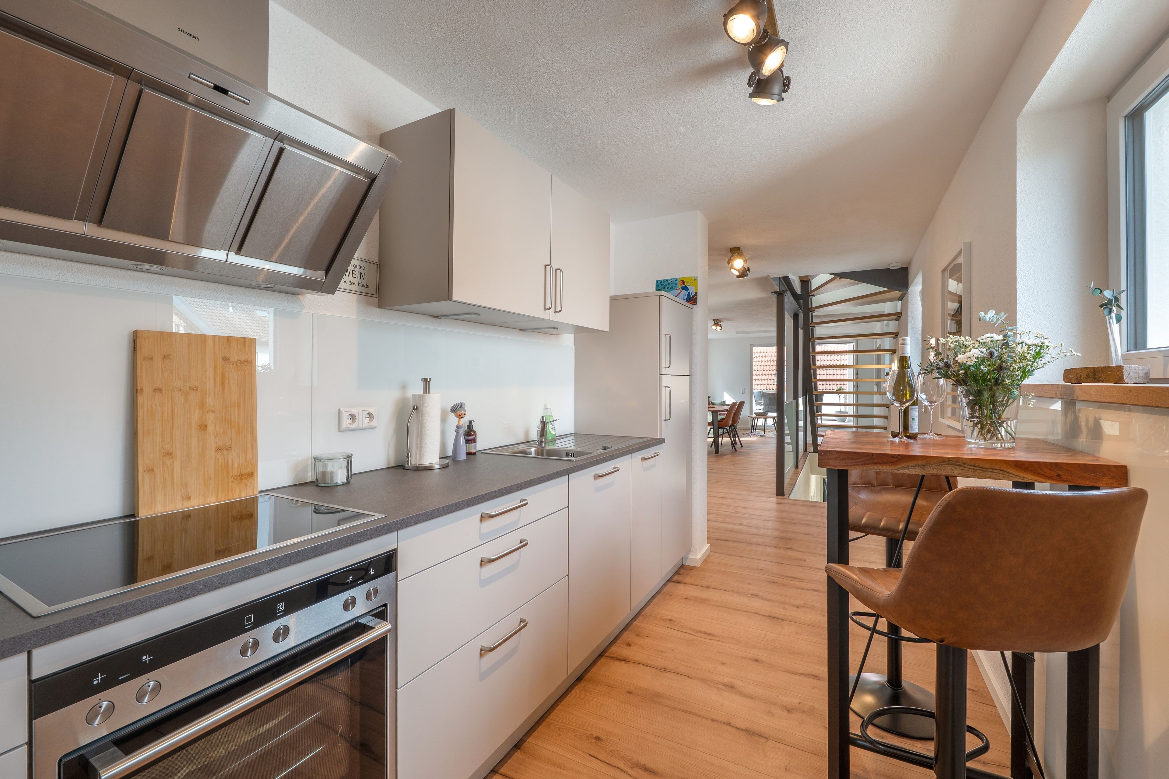 Een moderne keuken met roestvrijstalen apparatuur, houten vloeren en een bar met krukken.