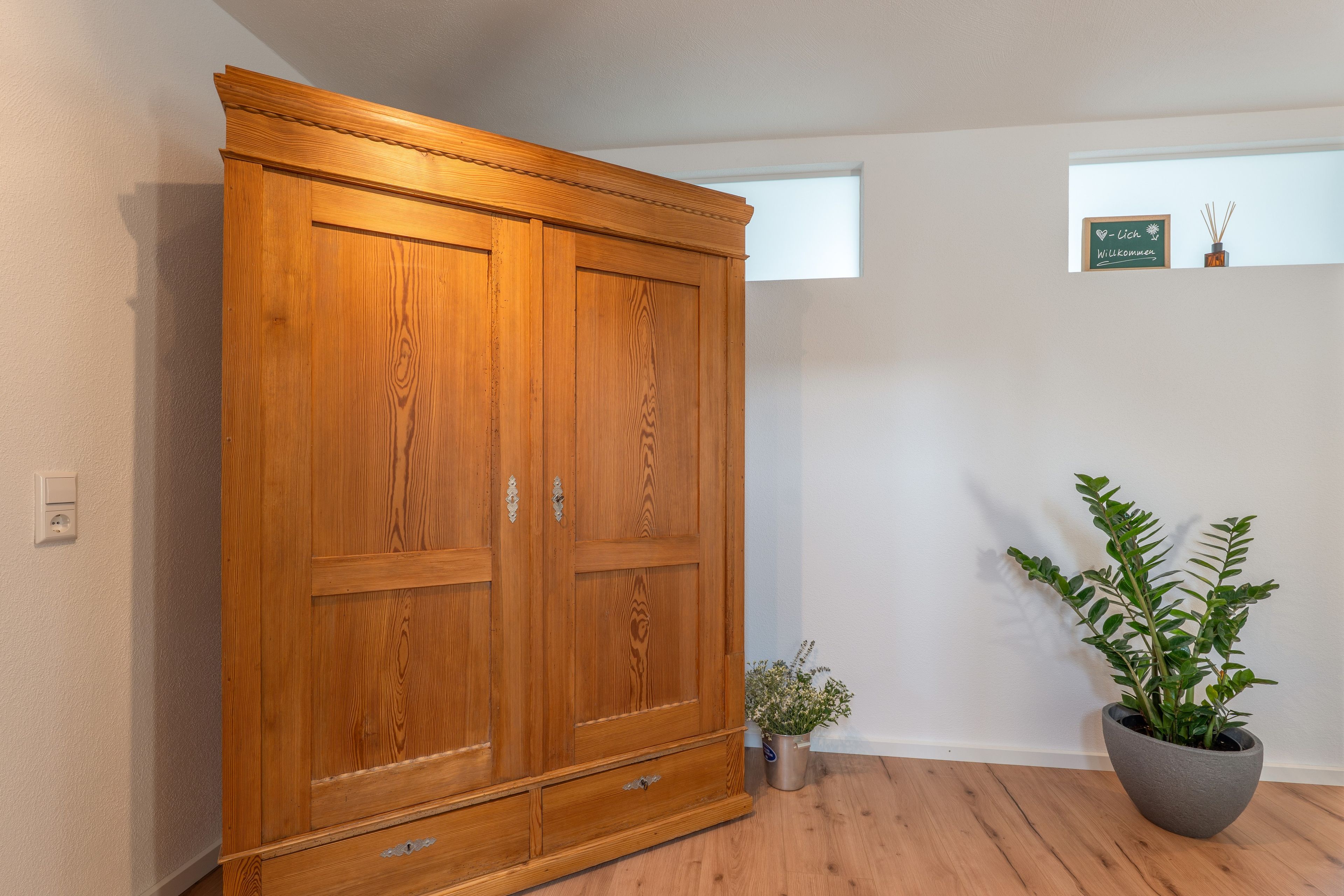 Ein Holzkleiderschrank mit zwei Türen und einer kleinen Pflanze daneben.