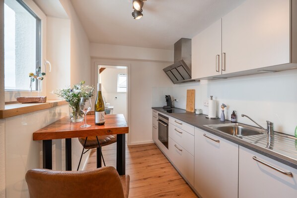 A modern kitchen with a wooden table, a wine bottle, and a vase of flowers.