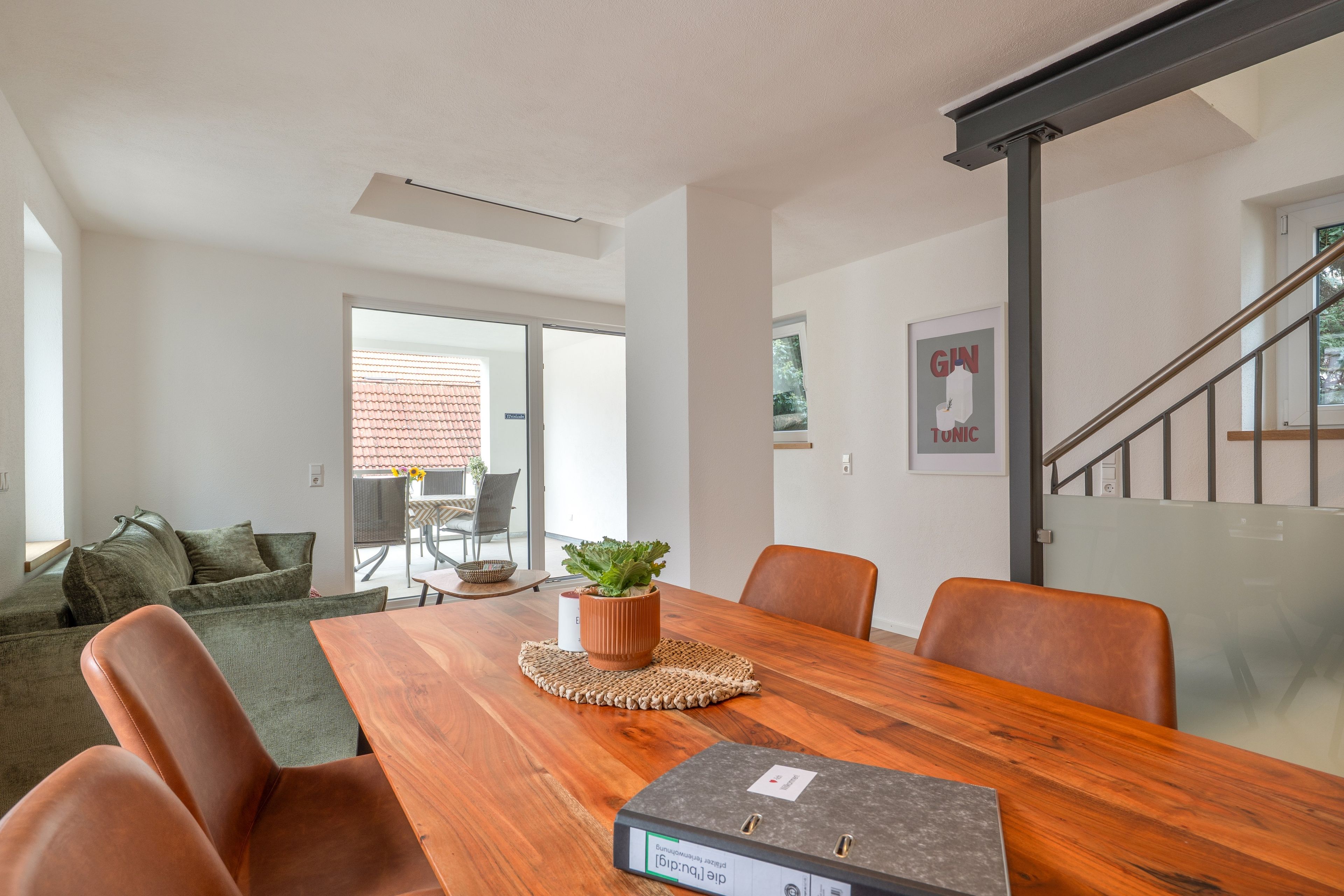A modern living room with a wooden dining table, leather chairs, a green sofa, and a potted plant.