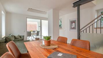 A modern living room with a wooden dining table, leather chairs, a green sofa, and a potted plant.