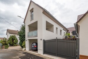 A two-story residential building with a balcony, a gated driveway, and a car parked inside.