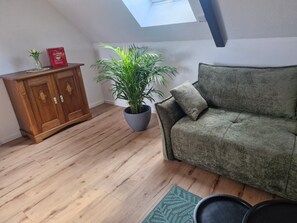 A room with a wooden cabinet, a green sofa, a potted plant, and a skylight.
