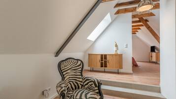 Een kamer met een stoel met een zebraprint, houten vloeren, een schuine plafond met zichtbare balken, een houten kast en een trap naar een hoger niveau.