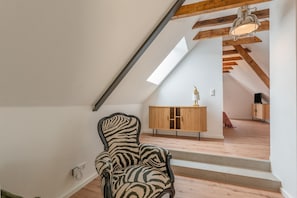 Una stanza con una poltrona a fantasia zebrata, pavimento in legno, soffitto a falda con travi a vista, un armadietto in legno e una scala che conduce a un livello superiore.