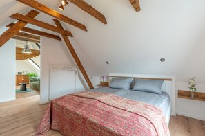 Une chambre avec un plafond en pente, un lit recouvert d’une couvre-lit à motifs et une petite table de chevet ornée d’un vase de fleurs.