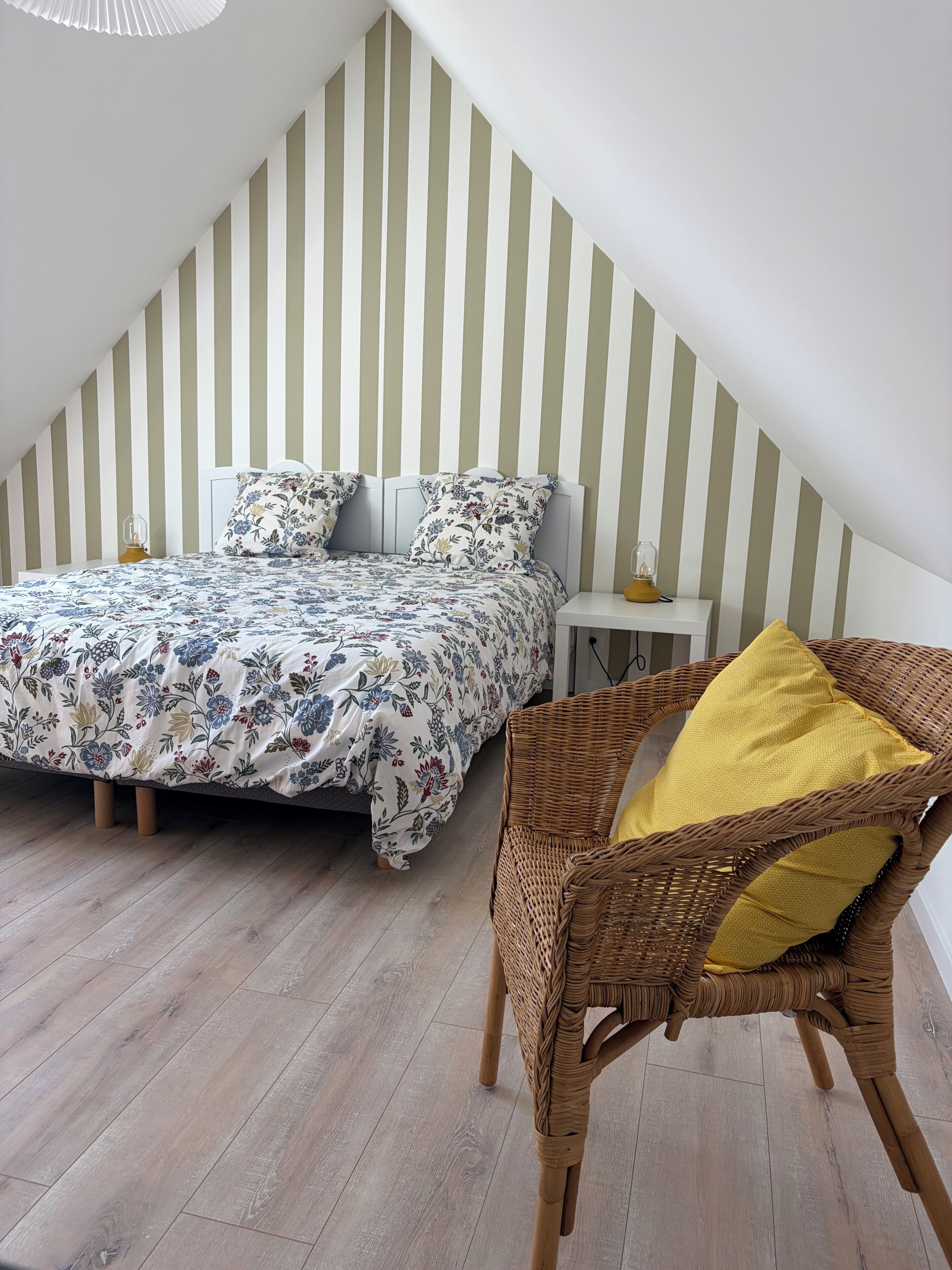 Quarto com cama, mesa de cabeceira, cadeira de vime e parede listrada.