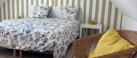 Ein Schlafzimmer mit einem Bett, einem Nachttisch, einem Korbstuhl und einer gestreiften Wand.