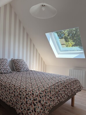 A bedroom with a sloped ceiling, a skylight, a bed with patterned bedding, and a white radiator. - Vrbo Property (Ploneour Lanvern)