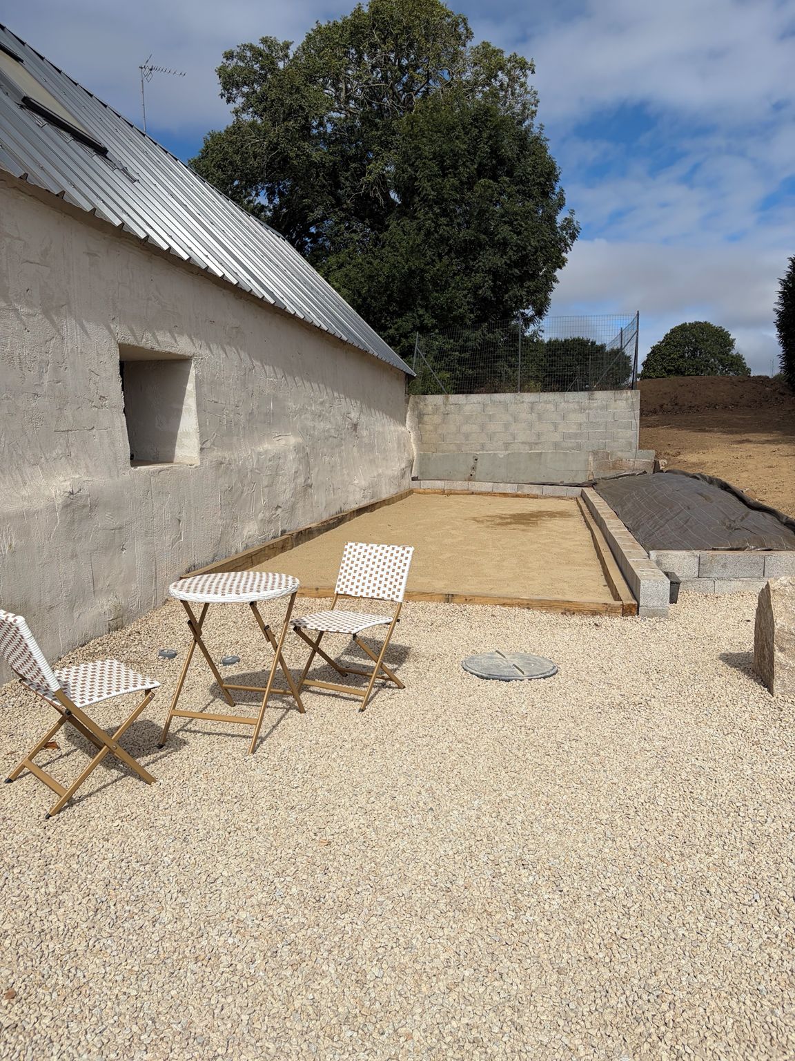 A gravel patio with a table and chairs, a concrete wall, and a metal roof.