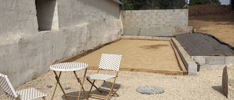 A gravel patio with a table and chairs, a concrete wall, and a metal roof.
