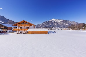 A large wooden building with a balcony, surrounded by a snowy landscape and mountains in the background. - Chiemgaujuwel Vacation Rental (Unterwössen)