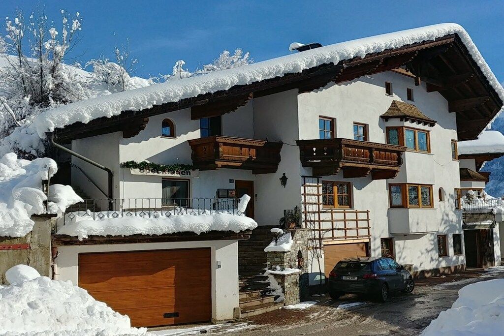 A two-story building with a wooden balcony, a garage, and a car parked in front.