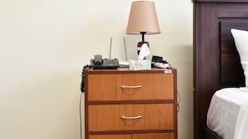 Una habitación de hotel con una mesita de noche de madera, una lámpara, un teléfono y una mesita de noche con una colcha blanca.