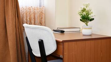 A wooden desk with a white chair, a remote control, a book, and a potted plant.